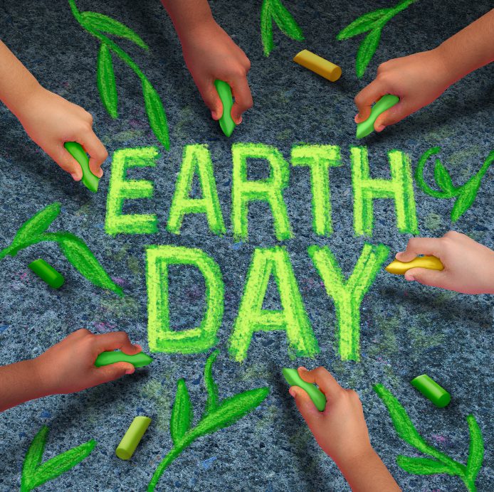 Earth day and environmental protection symbol as a group of diverse ethnic people coming together drawing text and leaves with green chalk on a pavement floor as a global community collaboration to save the planet.